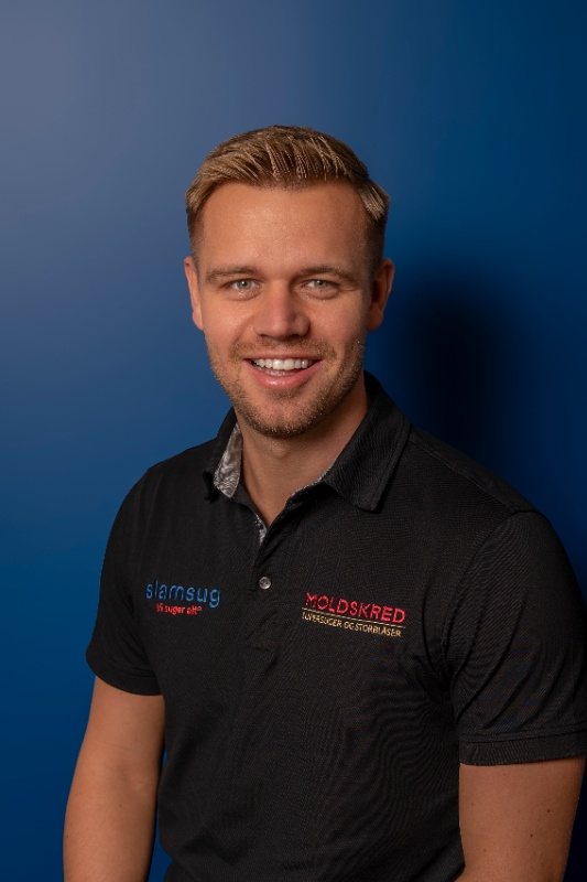 Mann med blondt hår og svart skjorte, foran blå bakgrunn